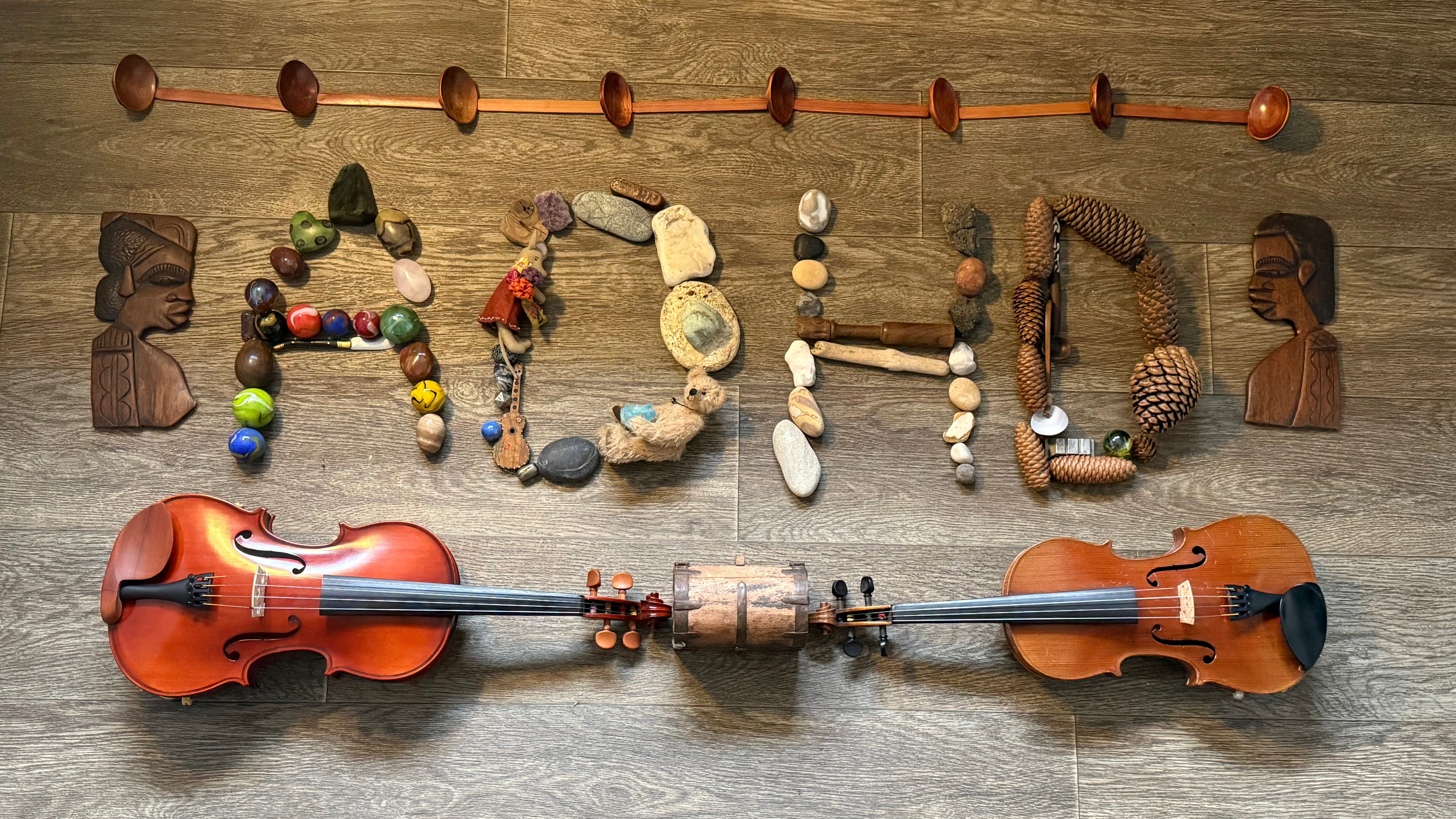 An artistic arrangement spelling 'ADHD' using various natural materials, wooden spoons, and two violins placed on a wooden floor.