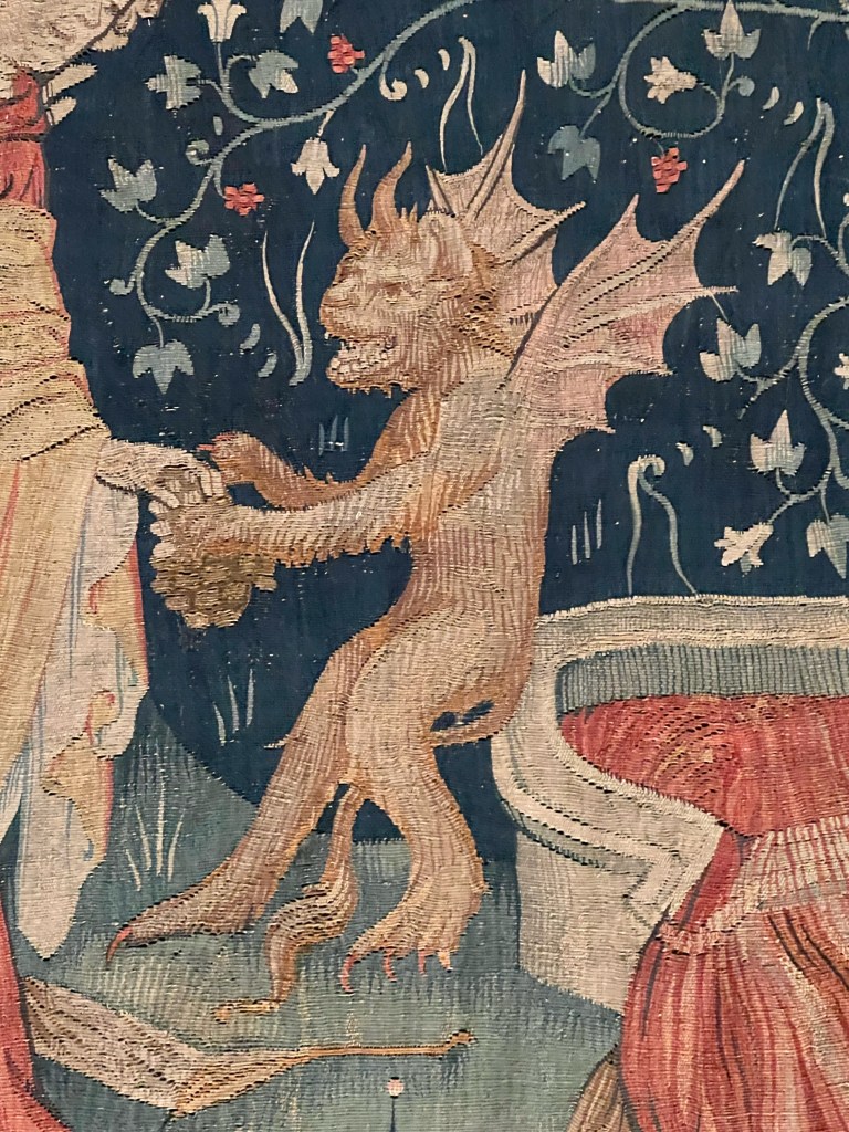 A detailed tapestry depicting a dragon-like creature with wings, interacting with a figure in medieval clothing, set against a floral background.