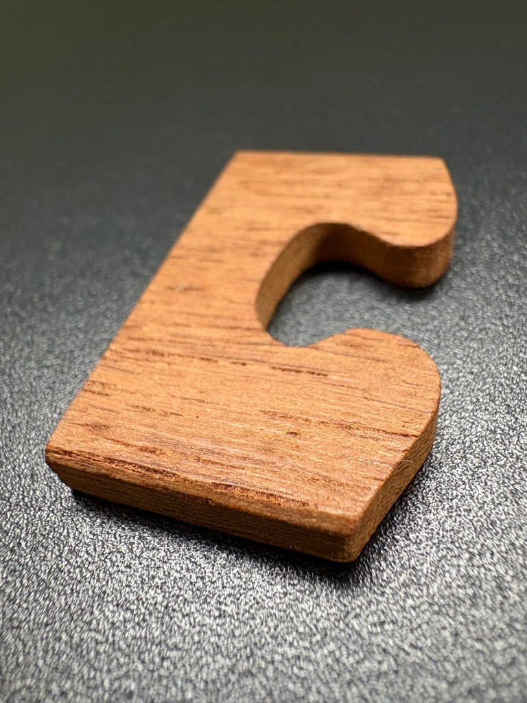 A wooden letter 'C' shaped block, resting on a dark surface.